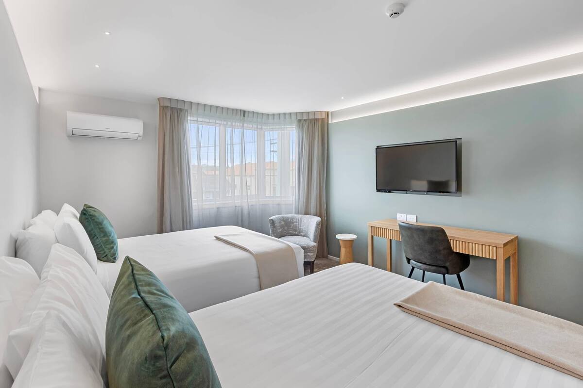 Camera d'albergo con due letti, una scrivania, una sedia, una TV e una finestra con tende.