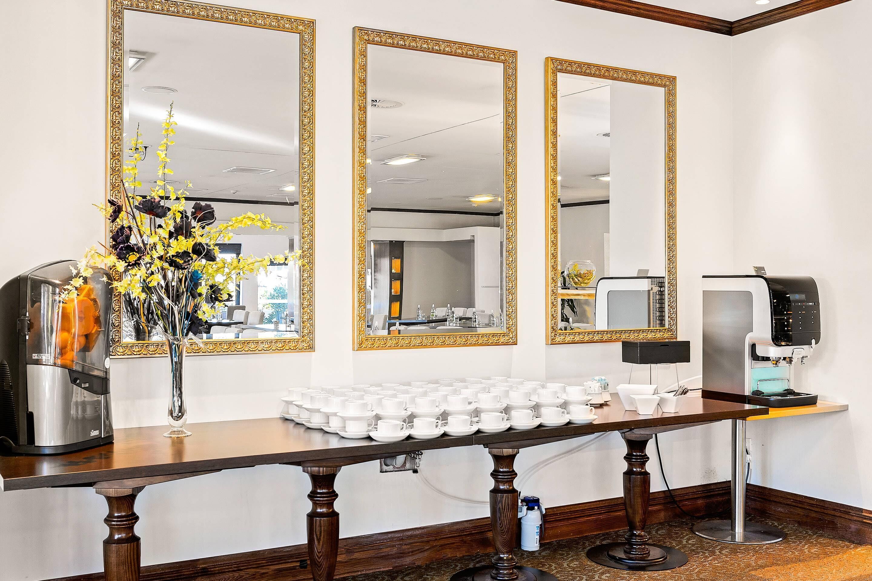 A reception area with a coffee machine, a vase with flowers, and a table with multiple cups.