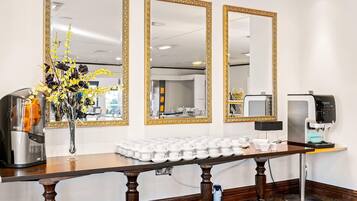 A reception area with a coffee machine, a vase with flowers, and a table with multiple cups.