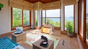 Un cuarto de spa con piso de madera, una camilla de masaje, una fuente de agua de madera y ventanas amplias con vista al mar.