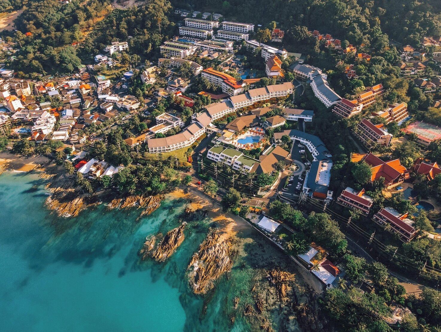 An aerial view of a coastal resort with multiple buildings, a swimming pool, and clear turquoise waters.