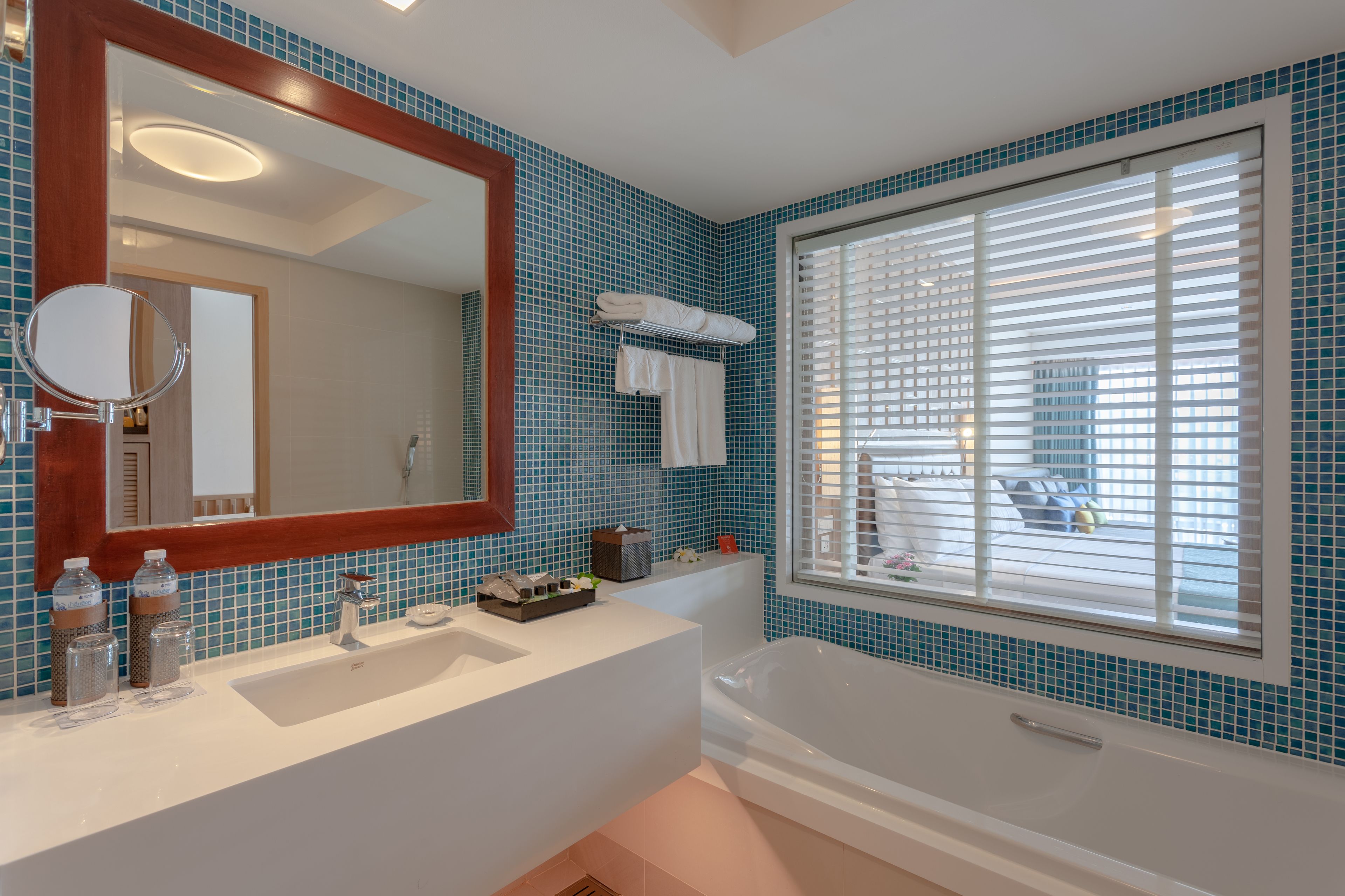 Ein Badezimmer mit einem großen Spiegel, einer Badewanne und einem Fenster mit Jalousien.