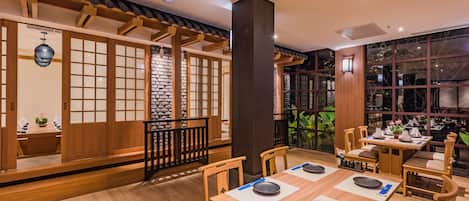 A traditional Japanese restaurant interior with tatami mat seating, wooden partitions, and a stone wall backdrop.