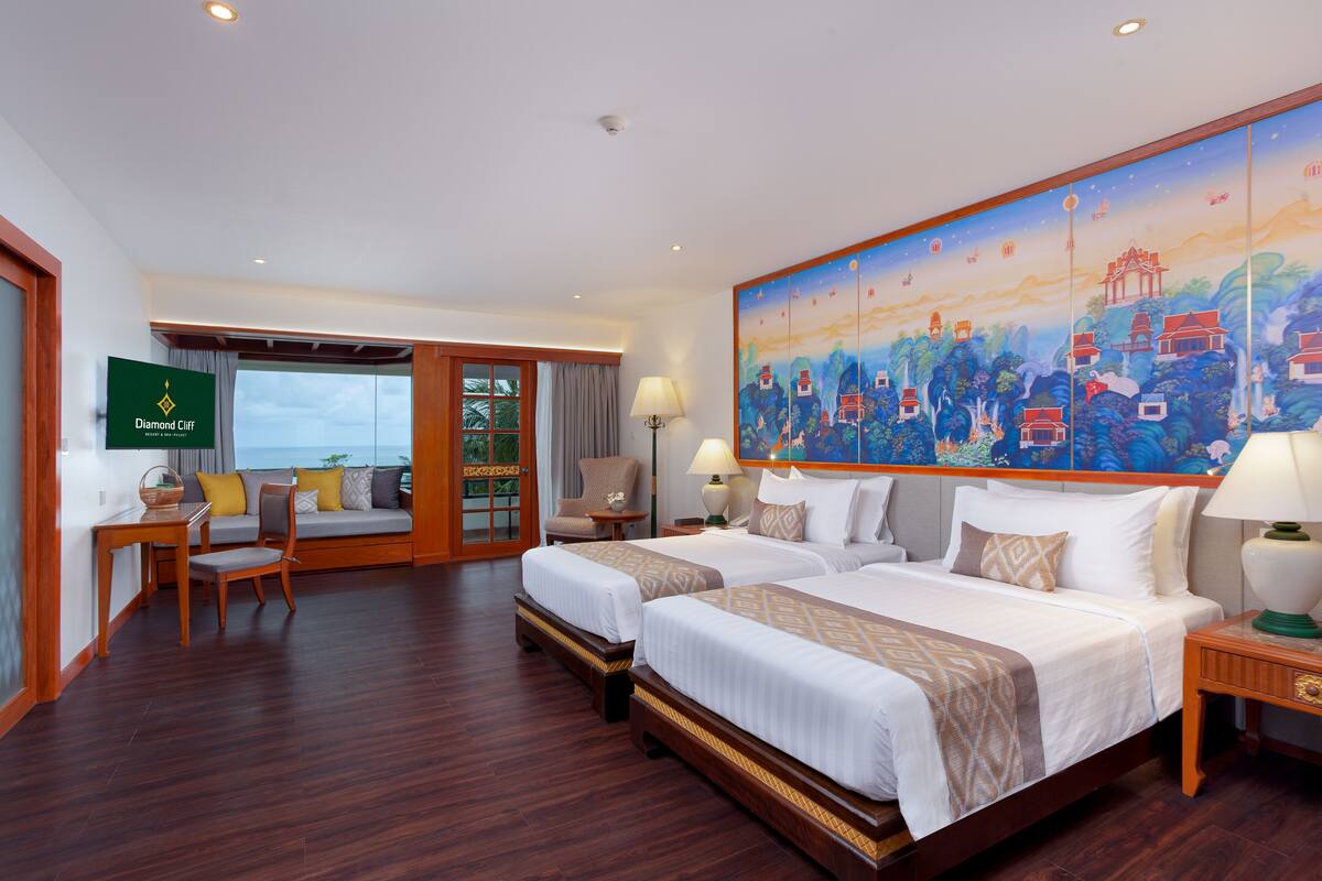 A hotel room with two beds, a TV, a painting, and a view of the sea.