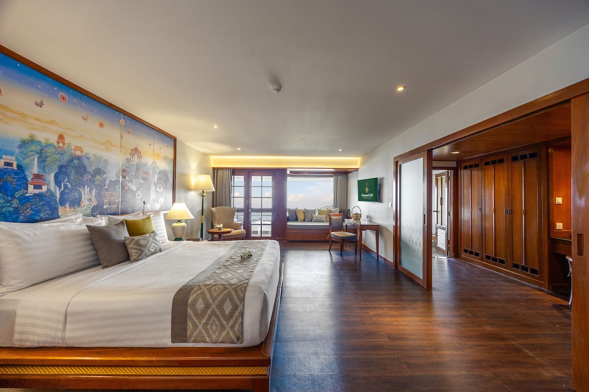 A hotel room with a large bed, a desk, a chair, a TV, and a view of the city.