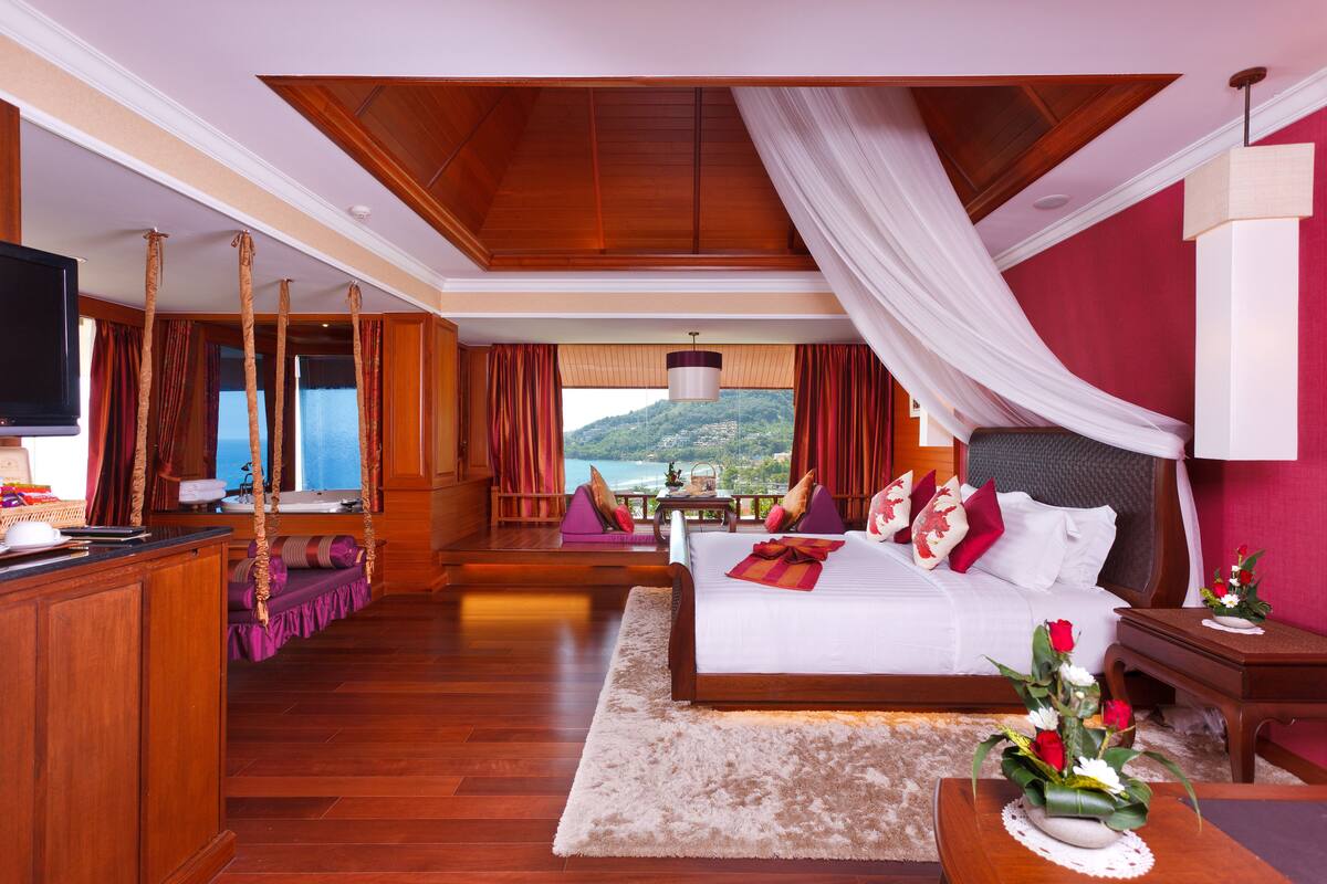 A spacious bedroom with a large bed, a television, a desk, and a view of the outdoors.