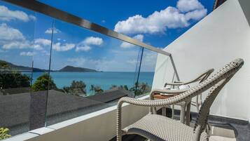 A balcony with a wicker chair, a glass railing, and a view of the ocean and a distant island.