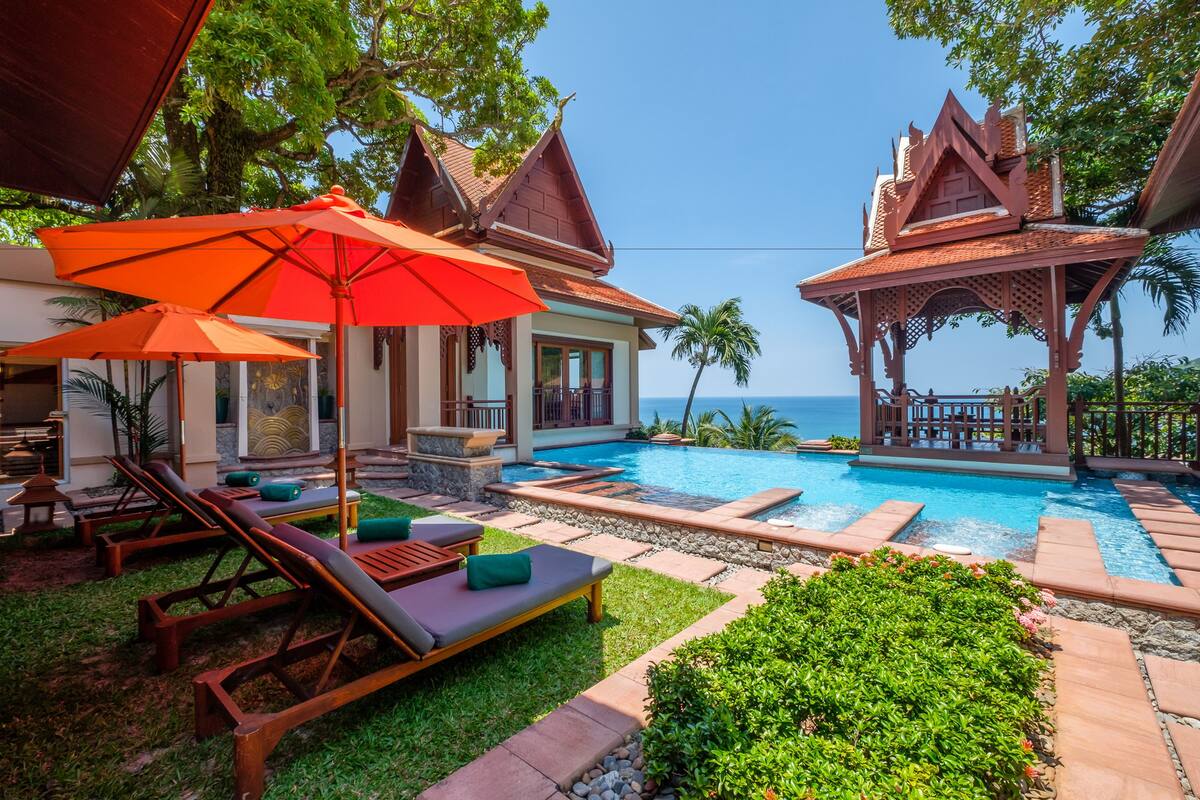 A pool area with lounge chairs and umbrellas, surrounded by tropical plants and a view of the ocean.