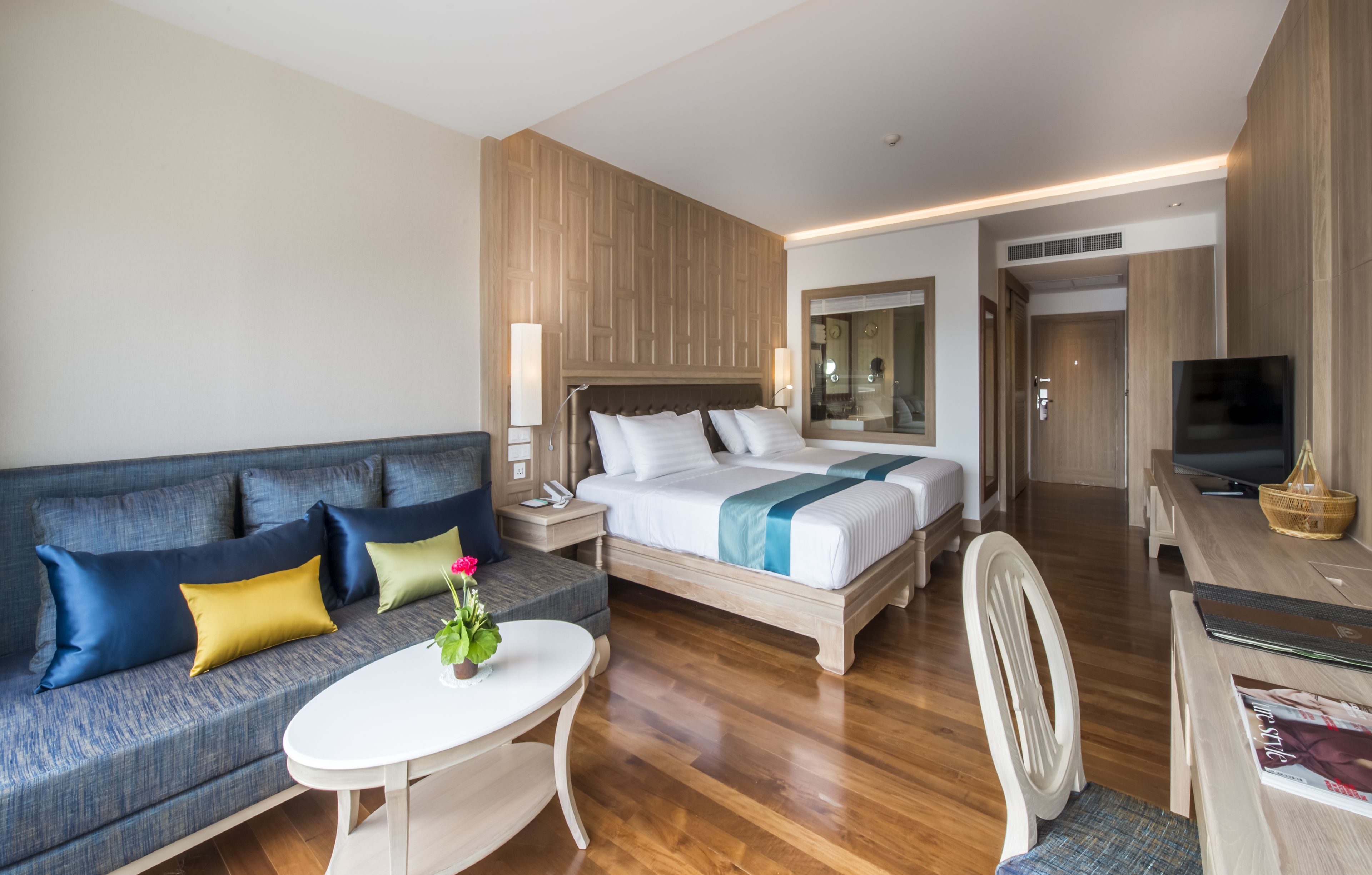 Una habitación de hotel moderna con una cama grande, un sofá, una mesita y un televisor.