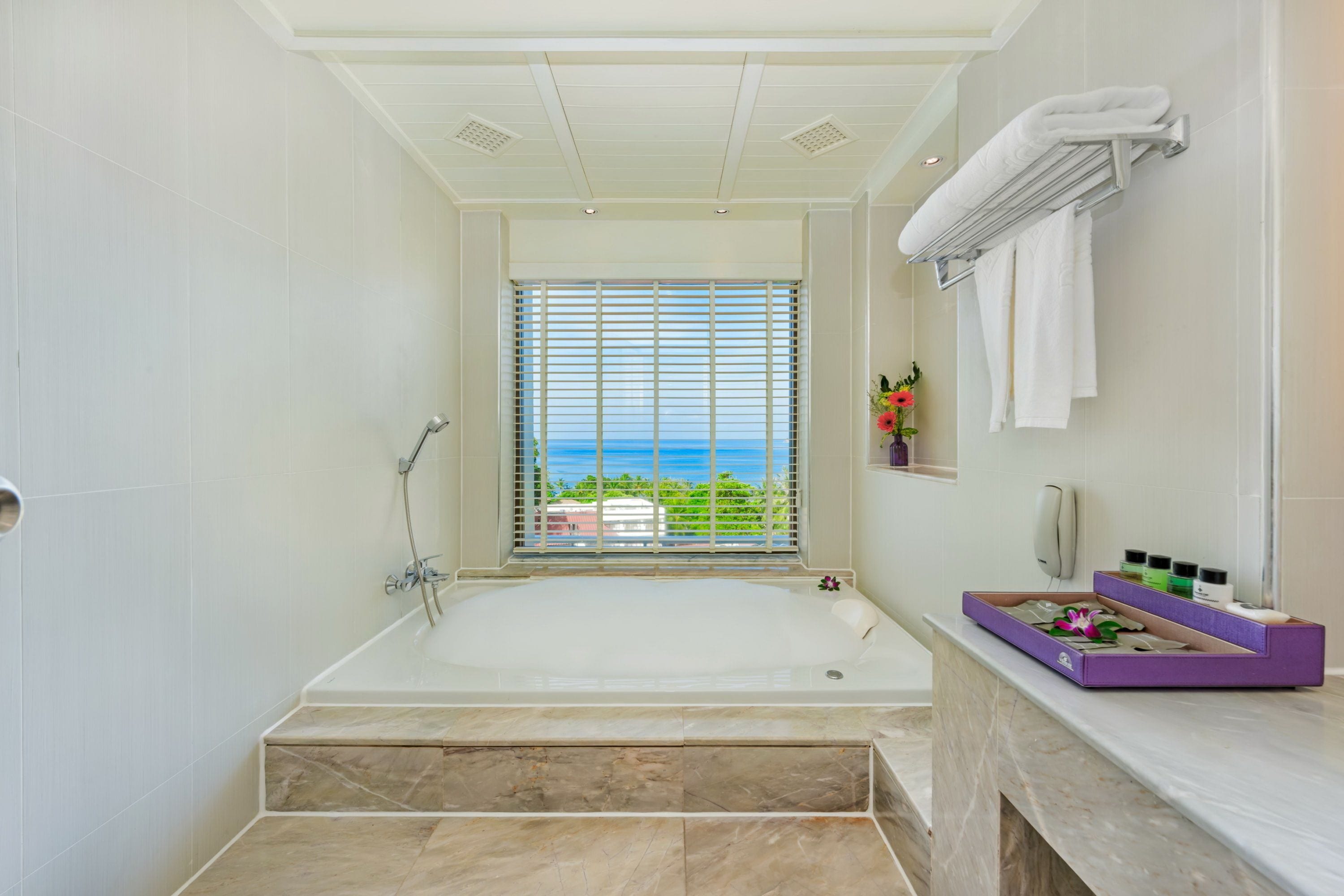 A modern bathroom with a large bathtub, a shower, and a view of the ocean through a window.