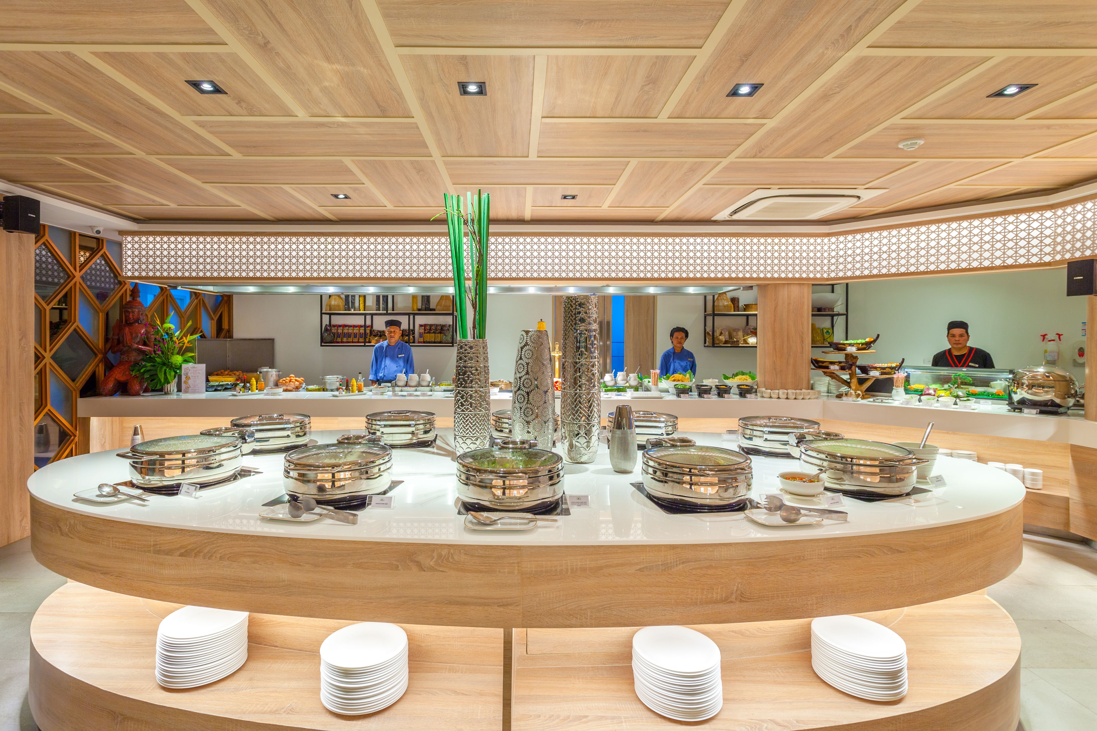 A buffet setup with various dishes and utensils, a decorative plant, and a patterned ceiling.