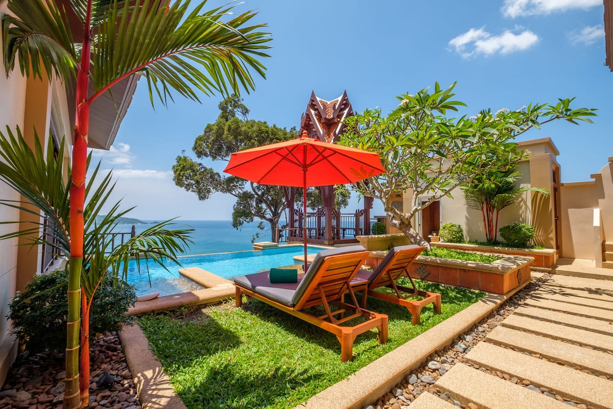 A poolside area with lounge chairs, a red umbrella, and a view of the ocean.