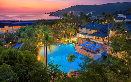 A resort with a large swimming pool surrounded by palm trees and lounge chairs.