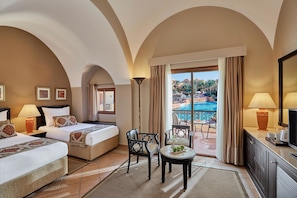 Ein Hotelzimmer mit zwei Betten, einer Sitzecke mit Tisch und Stühlen, einem Fernseher und Blick auf einen Swimmingpool.