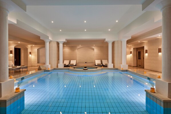 A large indoor swimming pool with a tiled floor, surrounded by white columns and walls, and equipped with seating and lighting. - Steigenberger Coraya Beach - Adults Friendly 16 Years Plus (El Quseir)