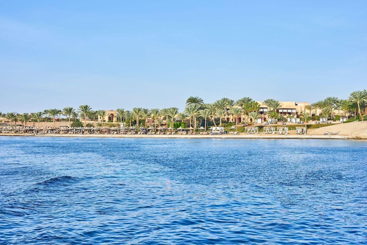 Un hotel frente al mar con vistas a la costa, palmeras y zona de piscina.