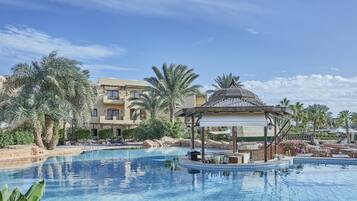 A swimming pool with a gazebo, palm trees, and a building with balconies in the background.