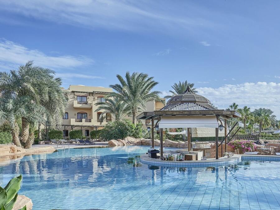 A swimming pool with a gazebo, palm trees, and a building with balconies in the background.