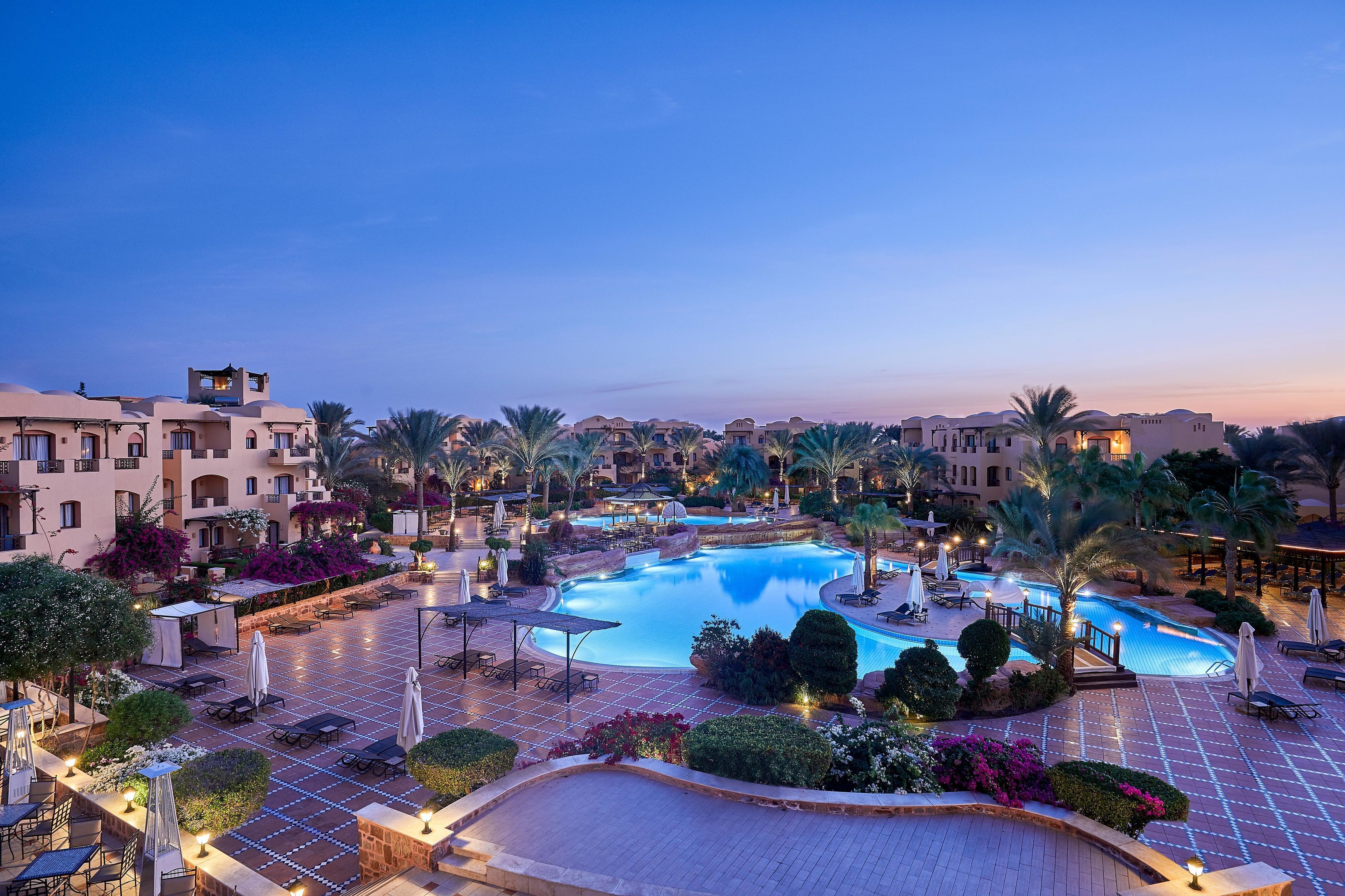 A resort with multiple swimming pools, palm trees, and outdoor seating areas.
