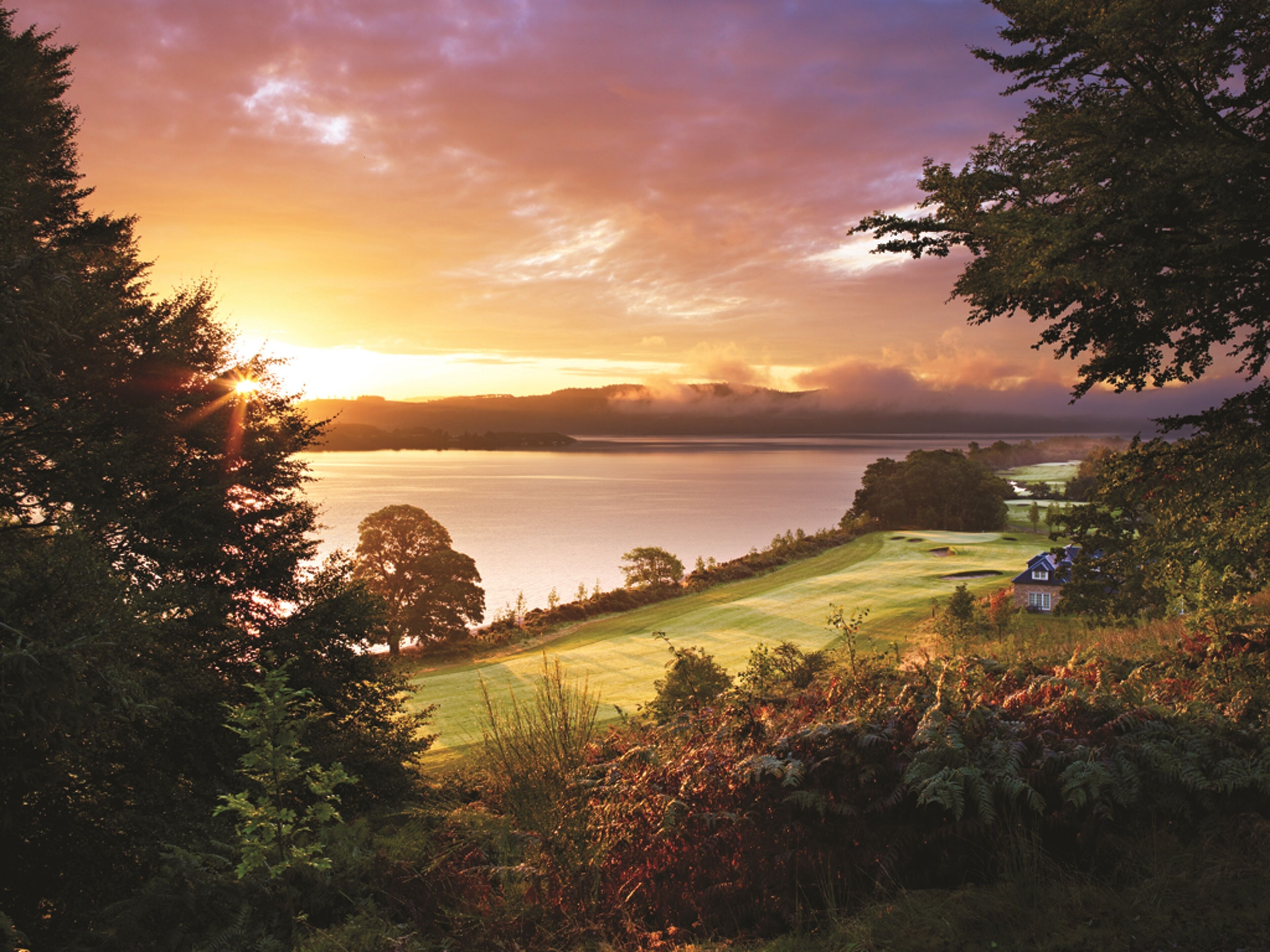 A coastal landscape with a golf course, a small house, and a body of water during sunset.