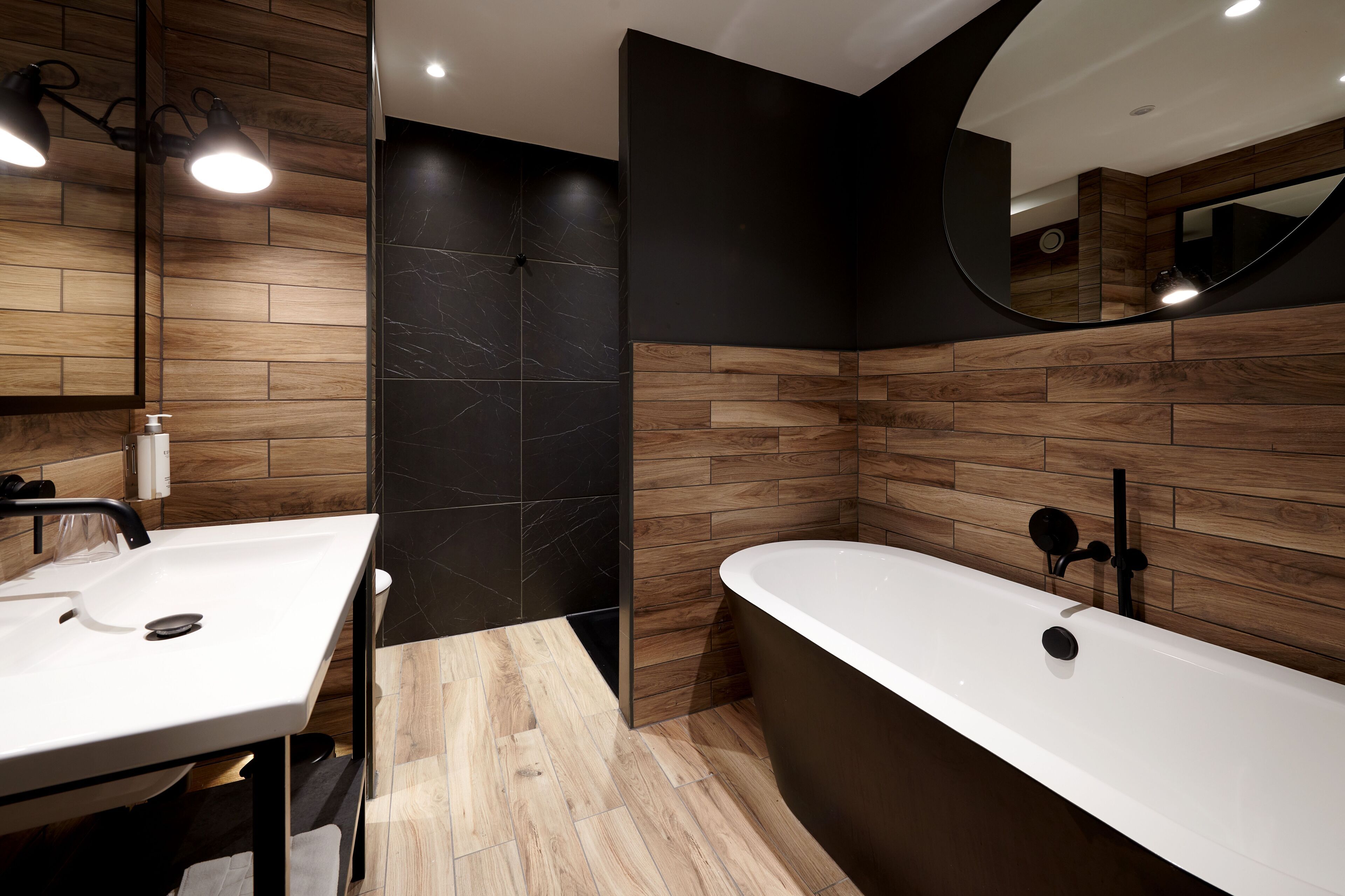 A modern bathroom with a wooden vanity, a freestanding bathtub, and a large mirror.