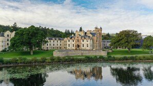 A large, historic building with a central courtyard and a reflective water body in front. - Cameron House on Loch Lomond (Alexandria)