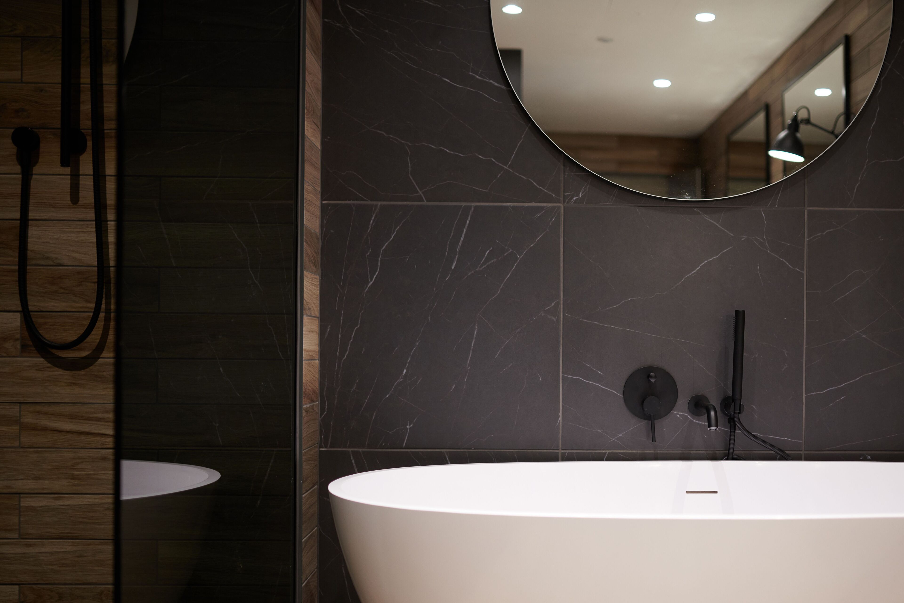 A modern bathroom with a freestanding bathtub, a round mirror, and a handheld showerhead.