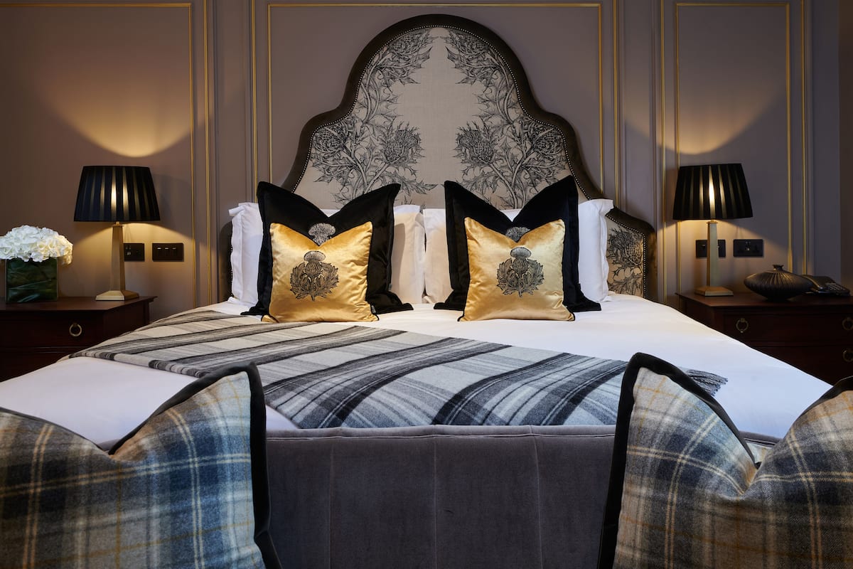 Una habitación de hotel con una cama grande, dos mesitas de noche, un cabecero con diseño floral y dos lámparas.