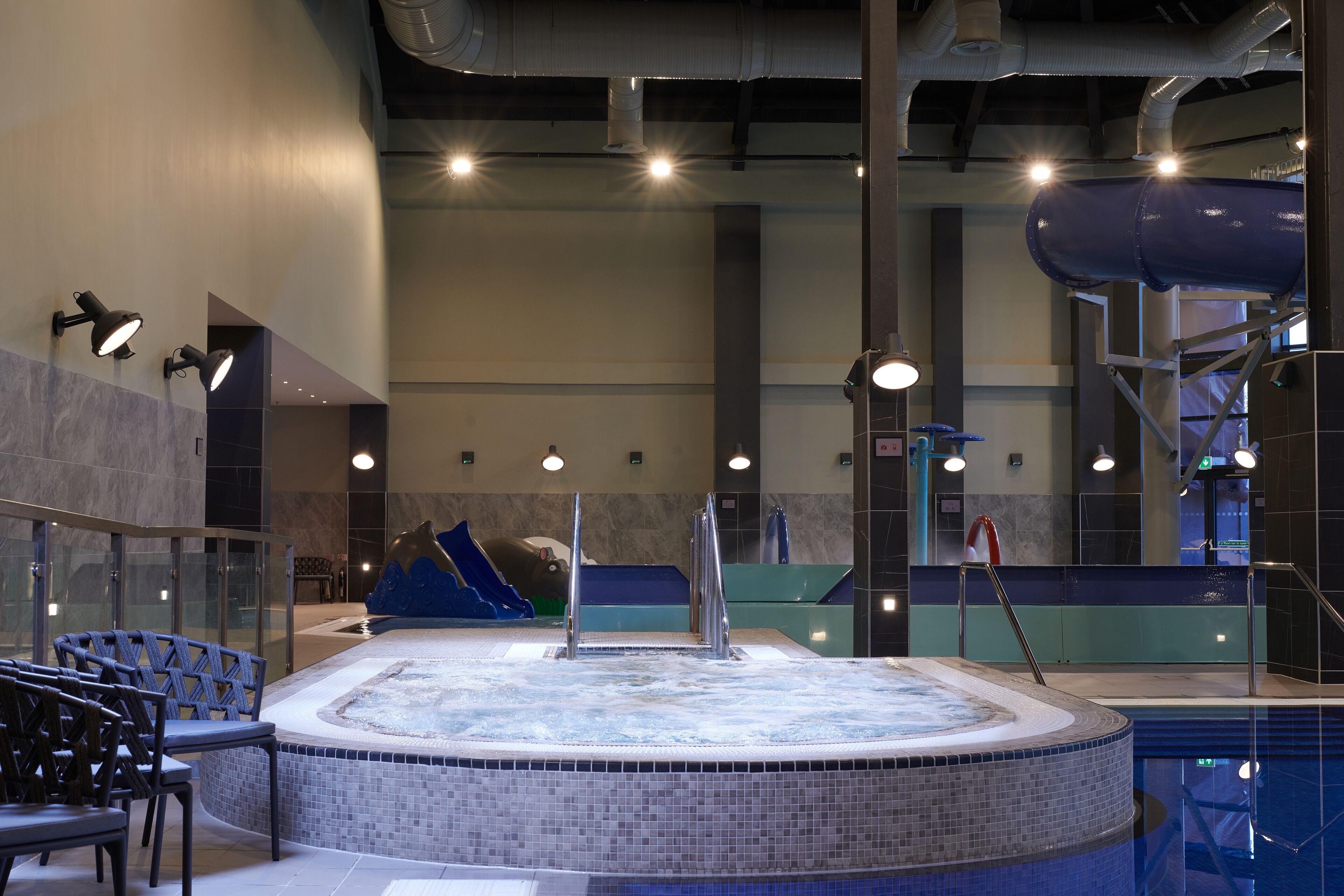 Une piscine intérieure moderne dotée d’un jacuzzi, d’un espace détente et d’un toboggan.