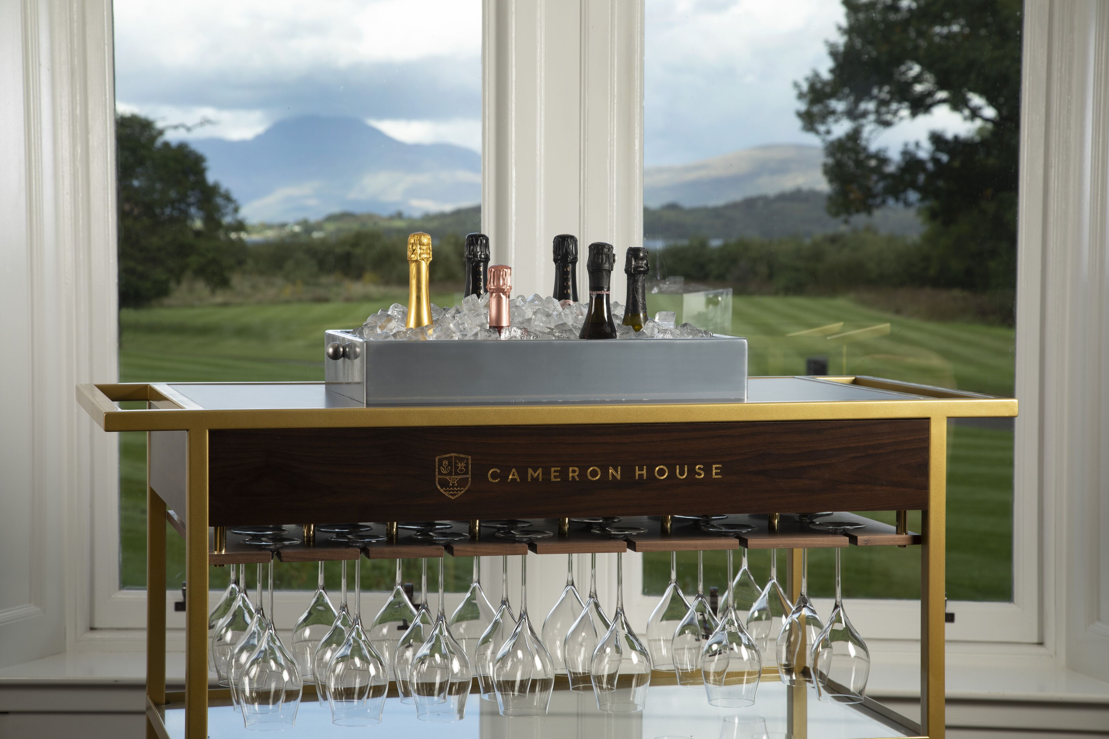 Une table avec une bouteille de champagne, des verres et une pancarte en bois sur laquelle on peut lire « Cameron House ».