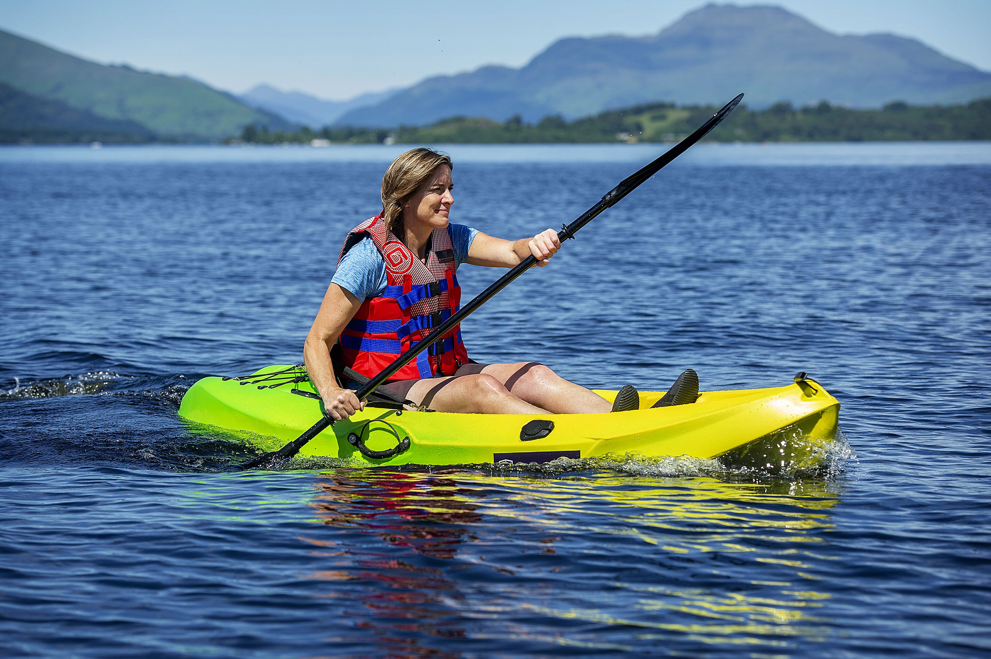 A person in a yellow kayak on a lake with mountains in the background.