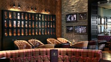 A bar area with a whiskey display, leather chairs, and a plaid sofa.