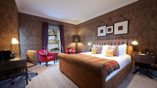 A hotel room with a large bed, a desk, two chairs, and a window with curtains. - Cameron House on Loch Lomond (Alexandria)