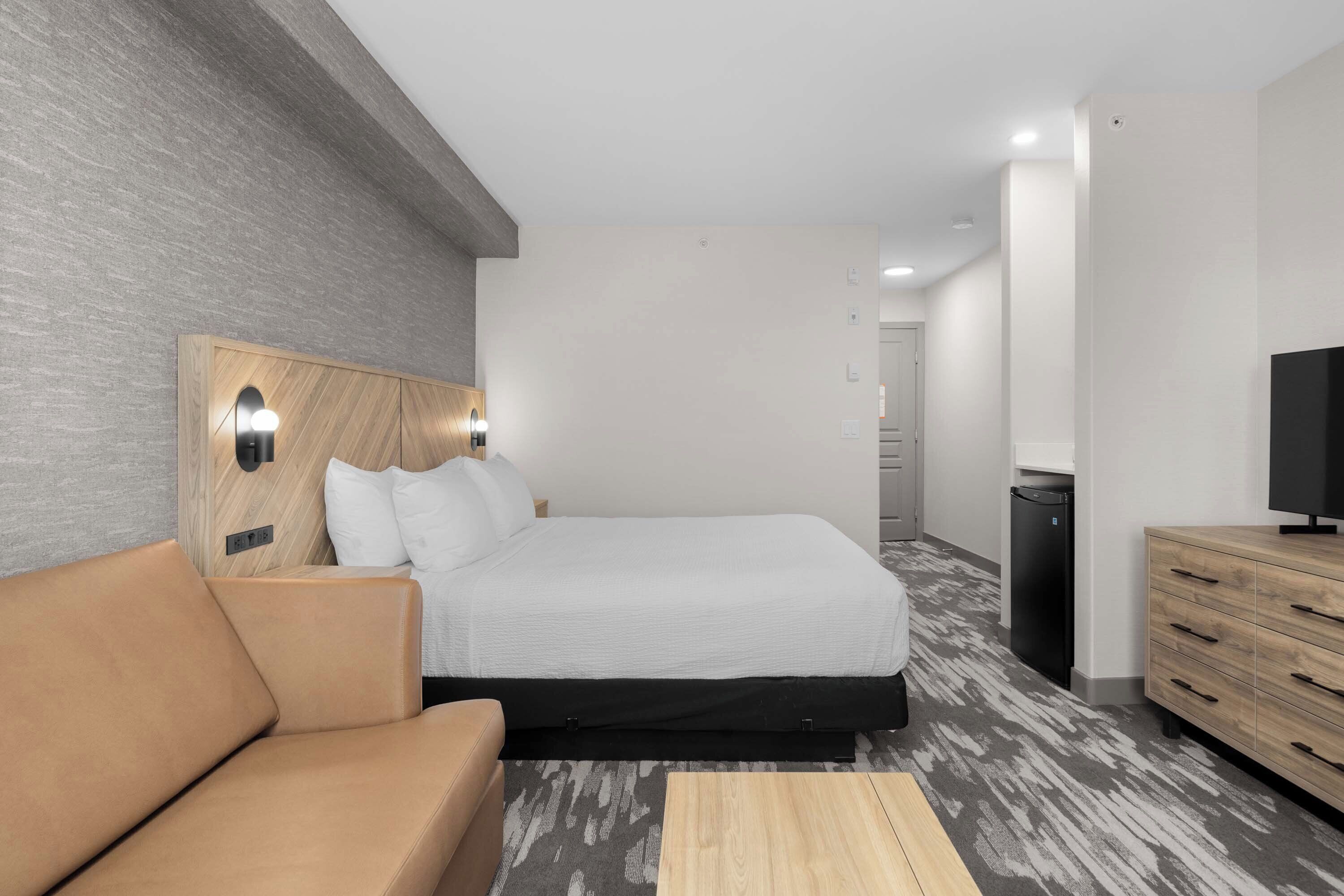 Une chambre d’hôtel moderne équipée d’un lit, d’un canapé, d’une télévision et d’une petite kitchenette.