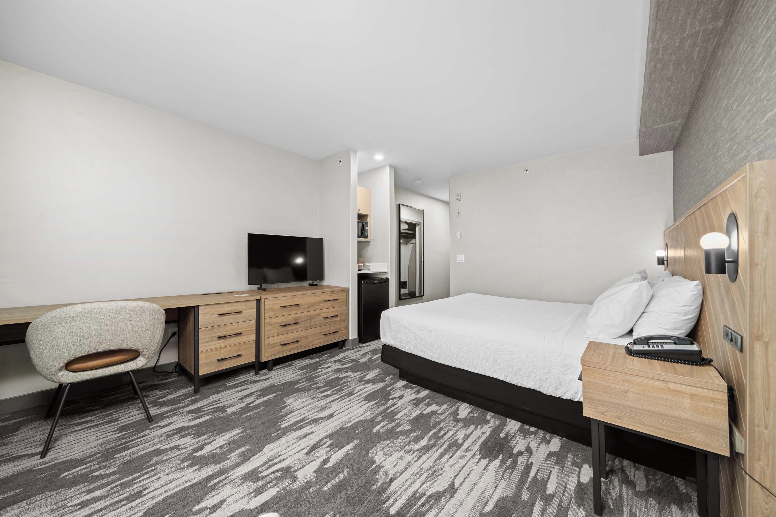 A modern hotel room with a bed, desk, chair, and a television.