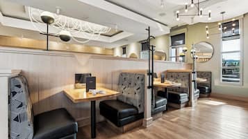 Interior moderno de restaurante com mesas de madeira e assentos estofados pretos, luminária no teto e uma grande janela com vista.