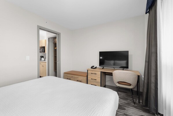 A hotel room with a bed, a desk with a television, a chair, and a wardrobe.