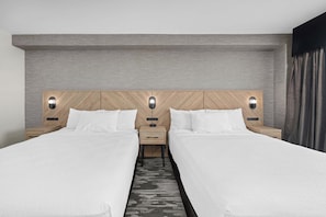 Habitación de hotel con dos camas, cabecero de madera, mesitas de noche con lámparas y una pared gris con textura.