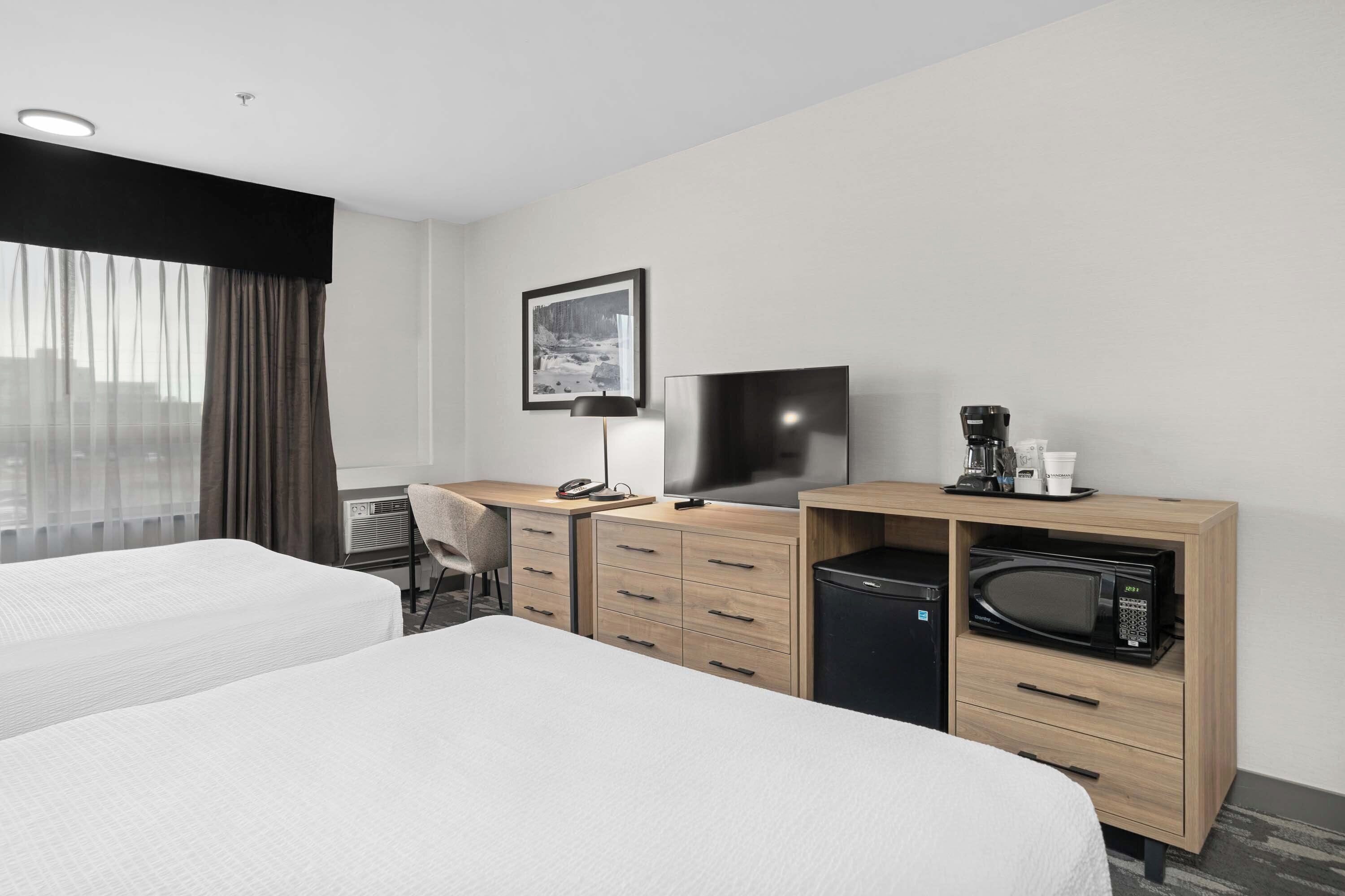 A hotel room with two beds, a desk with a TV, a microwave, and a coffee maker.