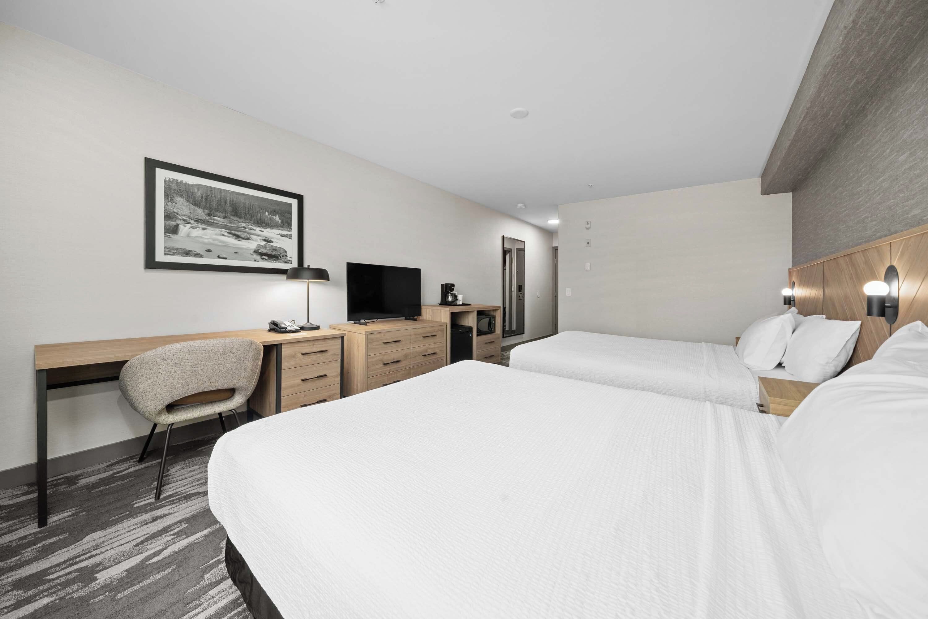 Ein Hotelzimmer mit zwei Betten, einem Schreibtisch mit Stuhl, einem Fernseher und einem gerahmten Bild an der Wand.