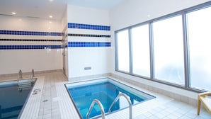 Une piscine intérieure avec des murs carrelés et une fenêtre laissant entrer la lumière naturelle.