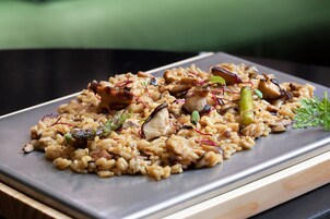 A plated dish of risotto with mushrooms and asparagus, garnished with microgreens and a sprig of parsley.