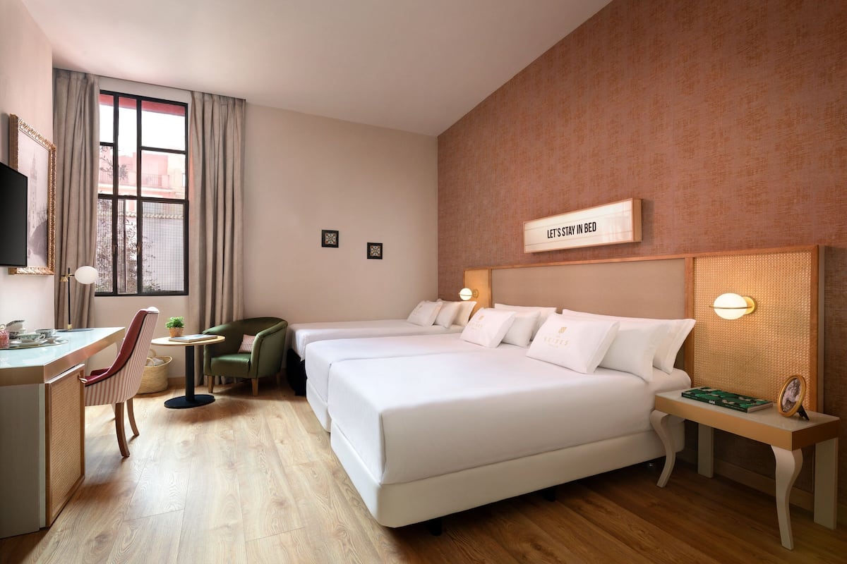 Hotellihuone, jossa on kaksi sänkyä, työpöytä, tuoli ja pieni pöytä.
