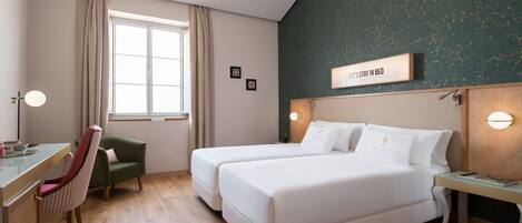 A hotel room with two beds, a desk, a chair, a window with curtains, and a sign on the wall.