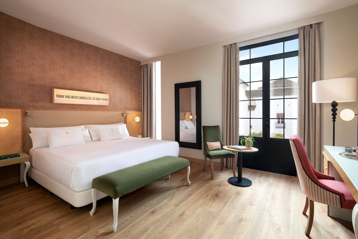 Hotellihuone, jossa on suuri sänky, pieni pöytä ja tuoli, työpöytä ja tuoli sekä suuri ikkuna, jossa on verhot.