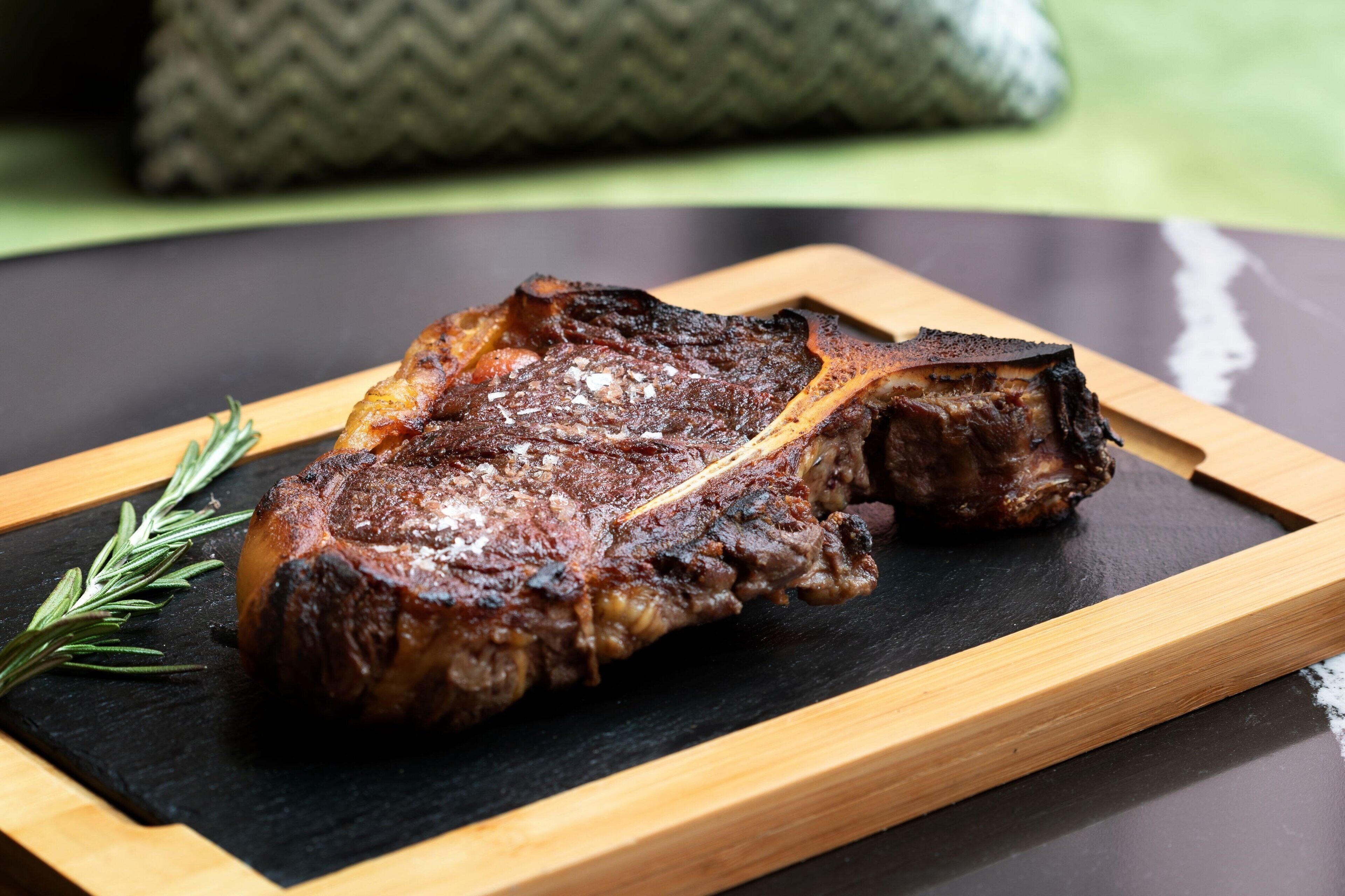 A steak on a wooden board with a sprig of rosemary.