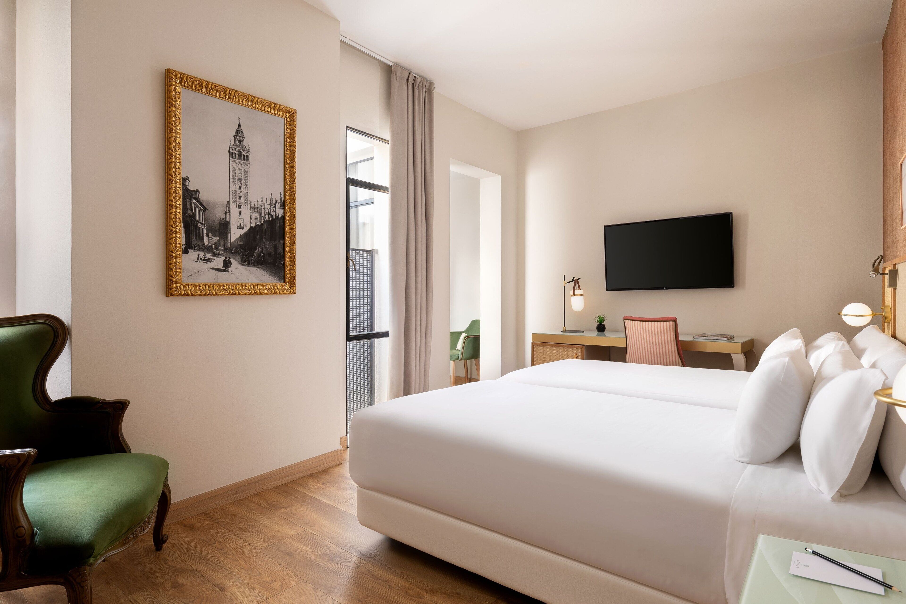 Habitación de hotel con una cama grande, un escritorio, una silla, un televisor y un cuadro en la pared.