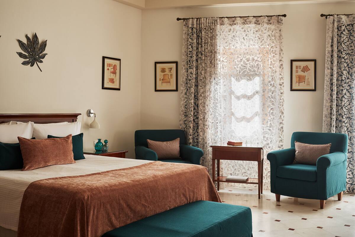 Ein Schlafzimmer mit einem Bett, zwei Sesseln, einem kleinen Tisch und Vorhängen.