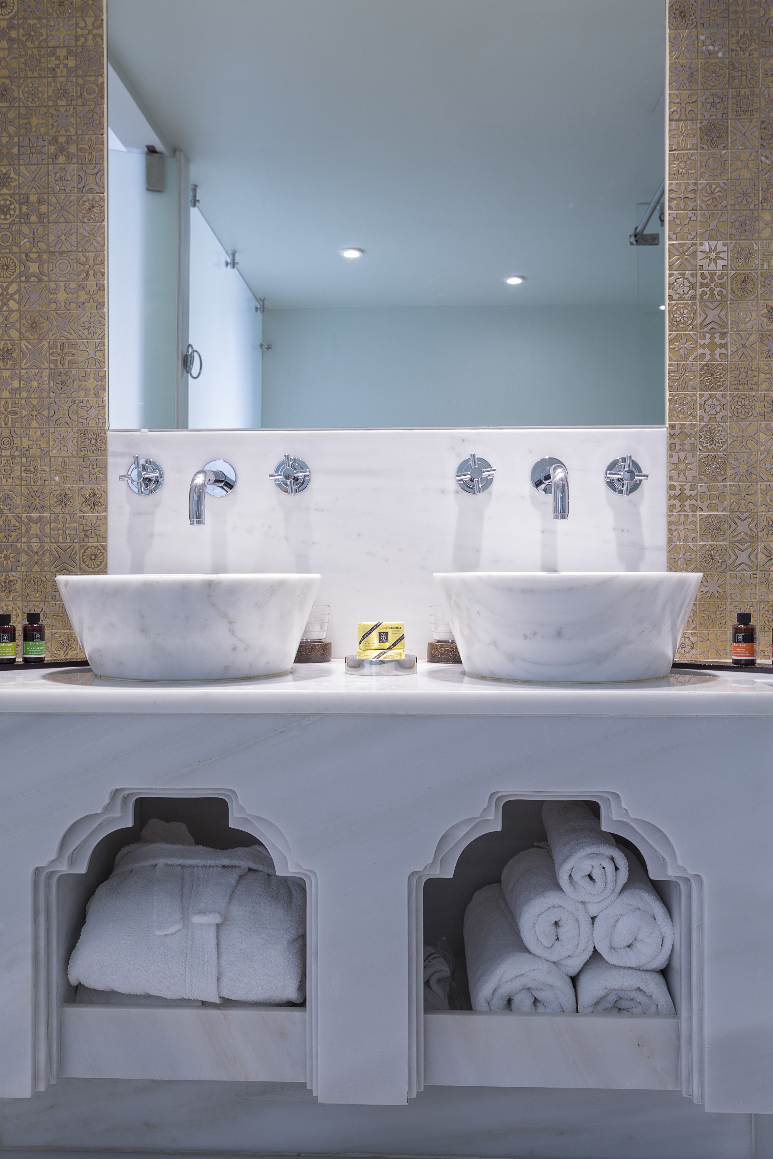 Une salle de bain avec deux vasques en marbre, un grand miroir et des rangements intégrés pour les serviettes.