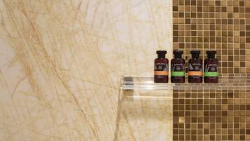 Cuatro botellas de productos para el cuidado corporal Apivita sobre una estantería en el baño.